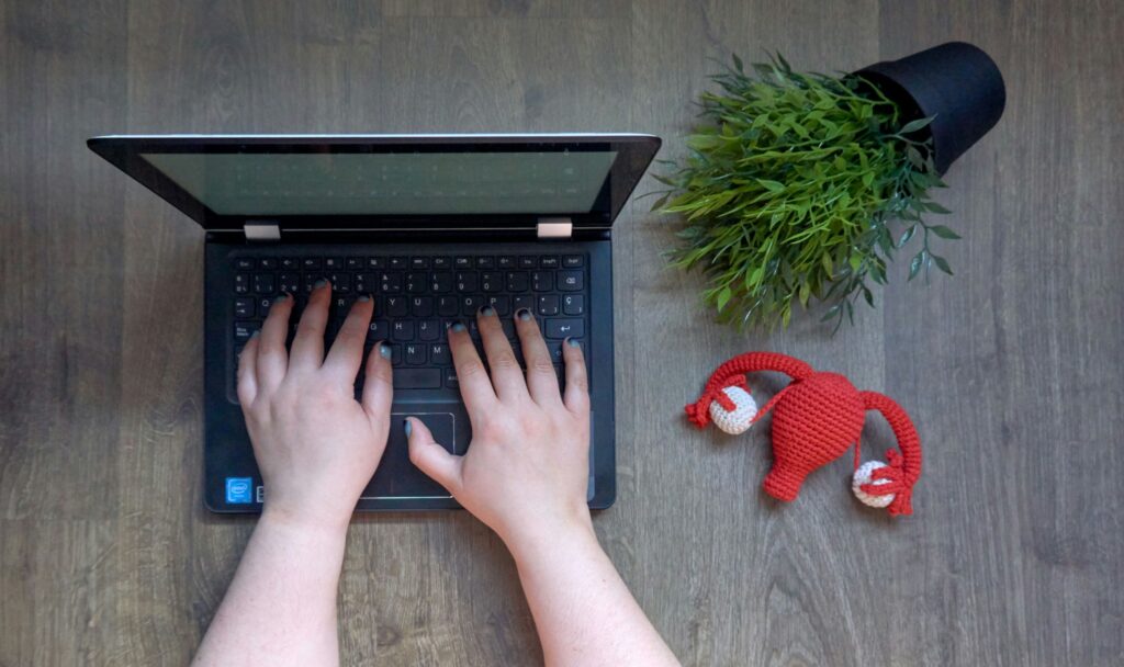 hands on a keyboard laptop next to a model of an enlarged uterus