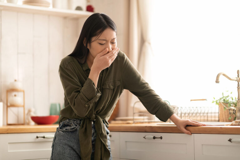 Woman with hand over mouth while standing in kitchen